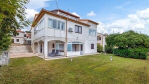 A two-story house with a stone facade, a balcony with seating, and a well-maintained lawn.