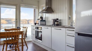 Et moderne køkken med hvide skabe, et rustfrit stål emhætte og udsigt til en sø gennem store vinduer.