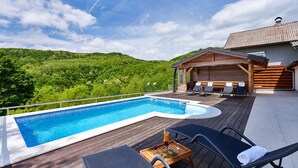 Ein Swimmingpool mit Liegestühlen und einer Holzterrasse, umgeben von üppiger Vegetation und einer Bergkulisse.
