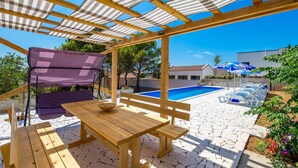 Eine Holz-Pergola mit Pool, Sitzgelegenheiten im Freien und blauem Himmel.