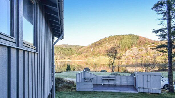 A house with a deck overlooking a lake and forested hills. - 3 bedroom lovely home in Helvik (Helvik)