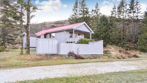 A small, single-story cabin with a red roof, surrounded by a wooden fence and a gravel driveway. - 3 bedroom lovely home in Helvik (Helvik)