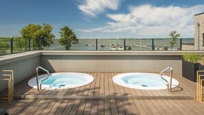 Terraço no telhado com duas banheiras de hidromassagem, um deck de madeira e vista para o porto e barcos.