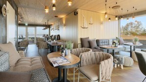 Um interior de restaurante moderno com tetos de madeira, luminárias pendentes suspensas e uma variedade de opções de assento, incluindo mesas e cadeiras acolchoadas.
