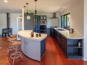 Eine moderne Küche mit Kochinsel, Barhocker, Herd, Backofen und großem Fenster.