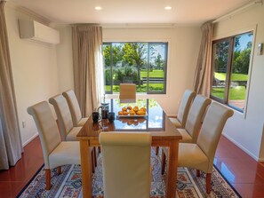 Un coin repas avec une table dressée pour quatre personnes, entourée de chaises, et donnant sur un jardin grâce à de grandes fenêtres.