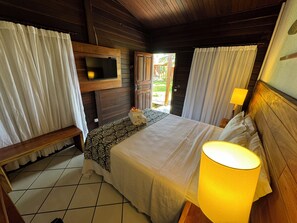 Un dormitorio tipo cabaña de madera con una cama, un televisor en la pared, un banco y una puerta que da al exterior.