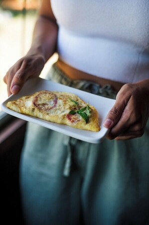 Henkilö pitää kädessään suorakaiteen muotoista valkoista lautasesta, jonka päällä on siivu pizzaa, joka on koristeltu yrteillä.