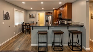 Una cocina moderna con una isla central, taburetes de madera y un comedor con mesa y sillas.