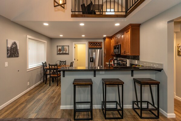 Una cocina moderna con una isla central, taburetes de madera y un comedor con mesa y sillas.