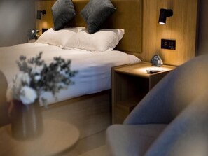 Ein modernes Hotelzimmer mit einem ordentlich bezogenen Bett, einem Nachttisch mit Lampe und einem kleinen Beistelltischchen mit Telefon.
