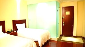 Een hotelkamer met twee bedden, een groene muur, een houten deur en een klein bureau met een telefoon.