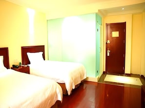 A hotel room with two beds, a green wall, a wooden door, and a small desk with a phone.