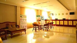 Een hotellobby met een receptiebalie, een zithoek met stoelen en een bank, en een groot raam met gordijnen.