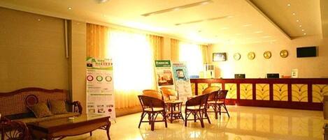 A hotel lobby with a reception desk, seating area with chairs and a sofa, and a large window with curtains.
