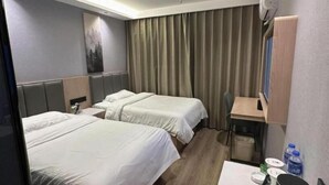 Habitación de hotel con dos camas, un escritorio, una silla, un cubo de basura y un televisor montado en la pared.