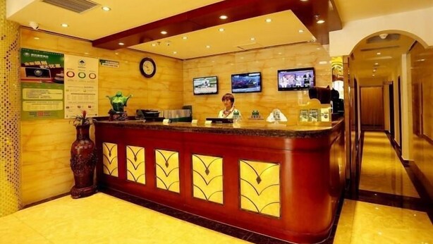 Zona de recepción de hotel con mostrador de mármol, una recepcionista y varias pantallas mostrando contenido.
