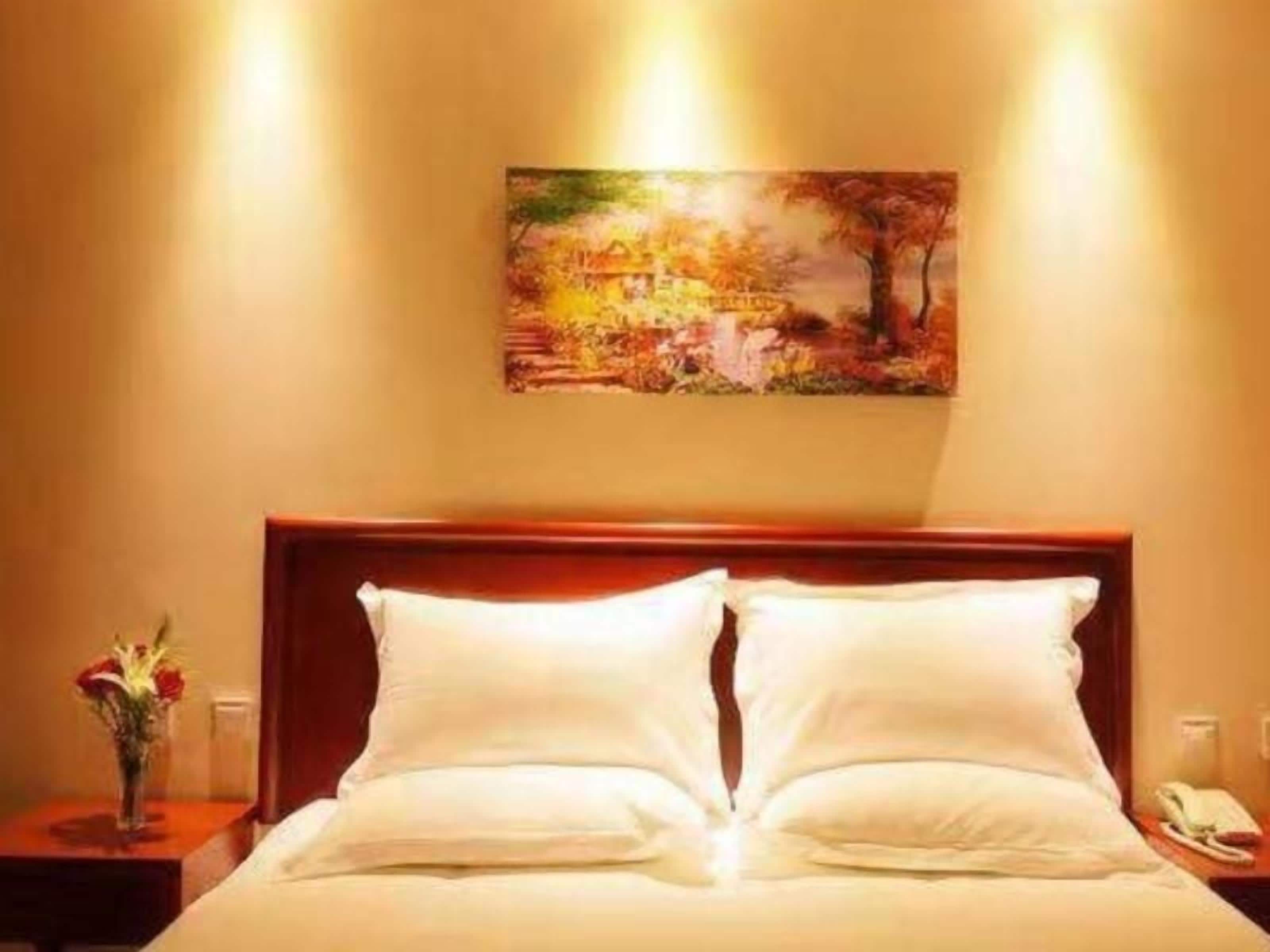A neatly made bed with white linens and a wooden headboard in a hotel room.