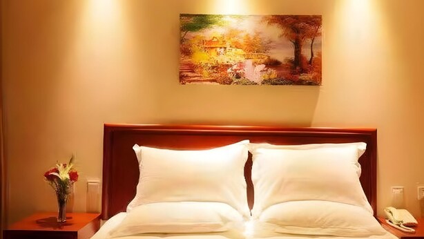 A hotel room with a bed, a nightstand, a vase of flowers, and a painting on the wall. - Greentree Inn Chifeng Linxi Ronglin Homeland Express Hotel (Chifeng)