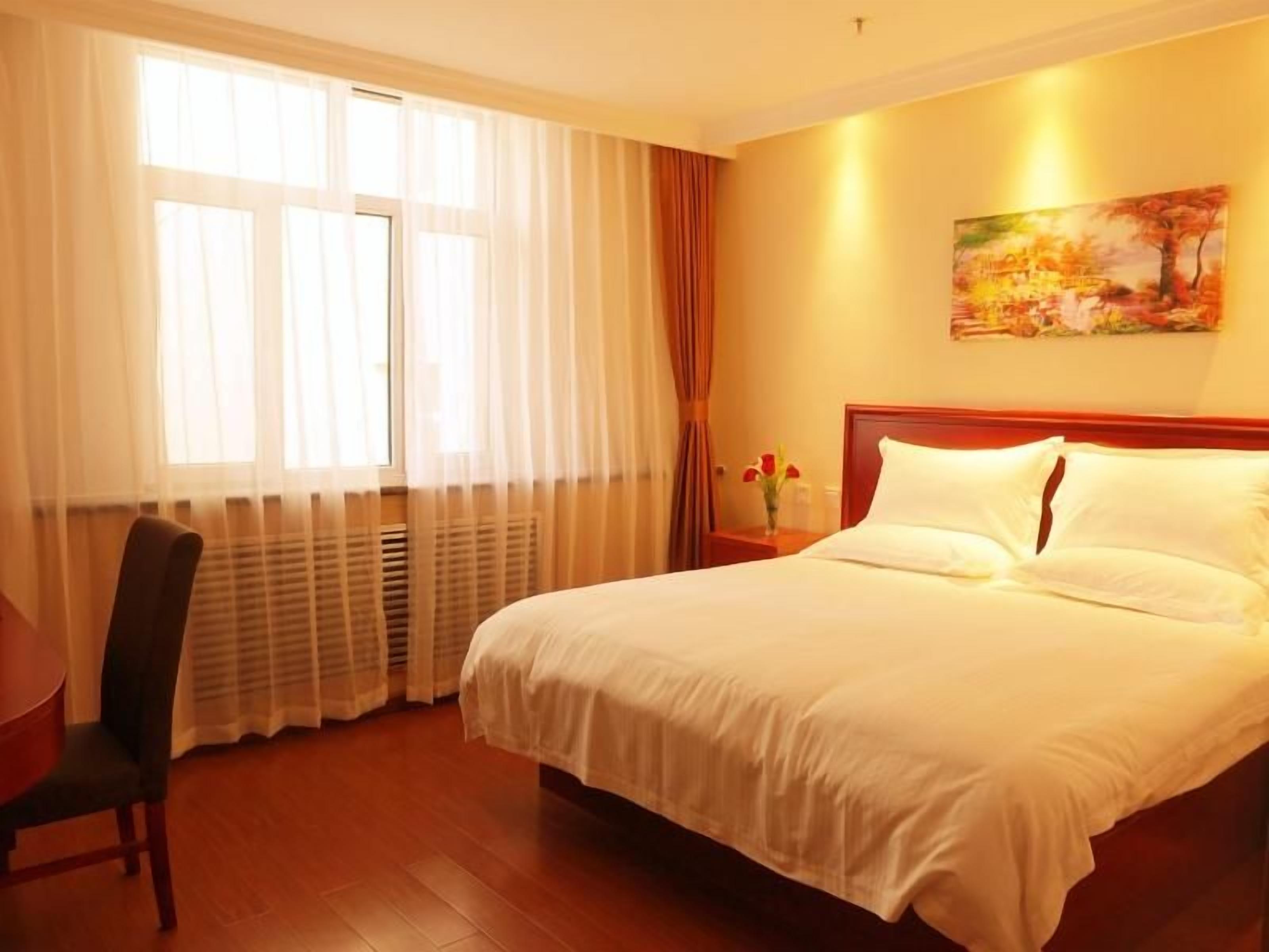 A hotel room with a large bed, a chair, a nightstand with a vase of flowers, and a painting on the wall.