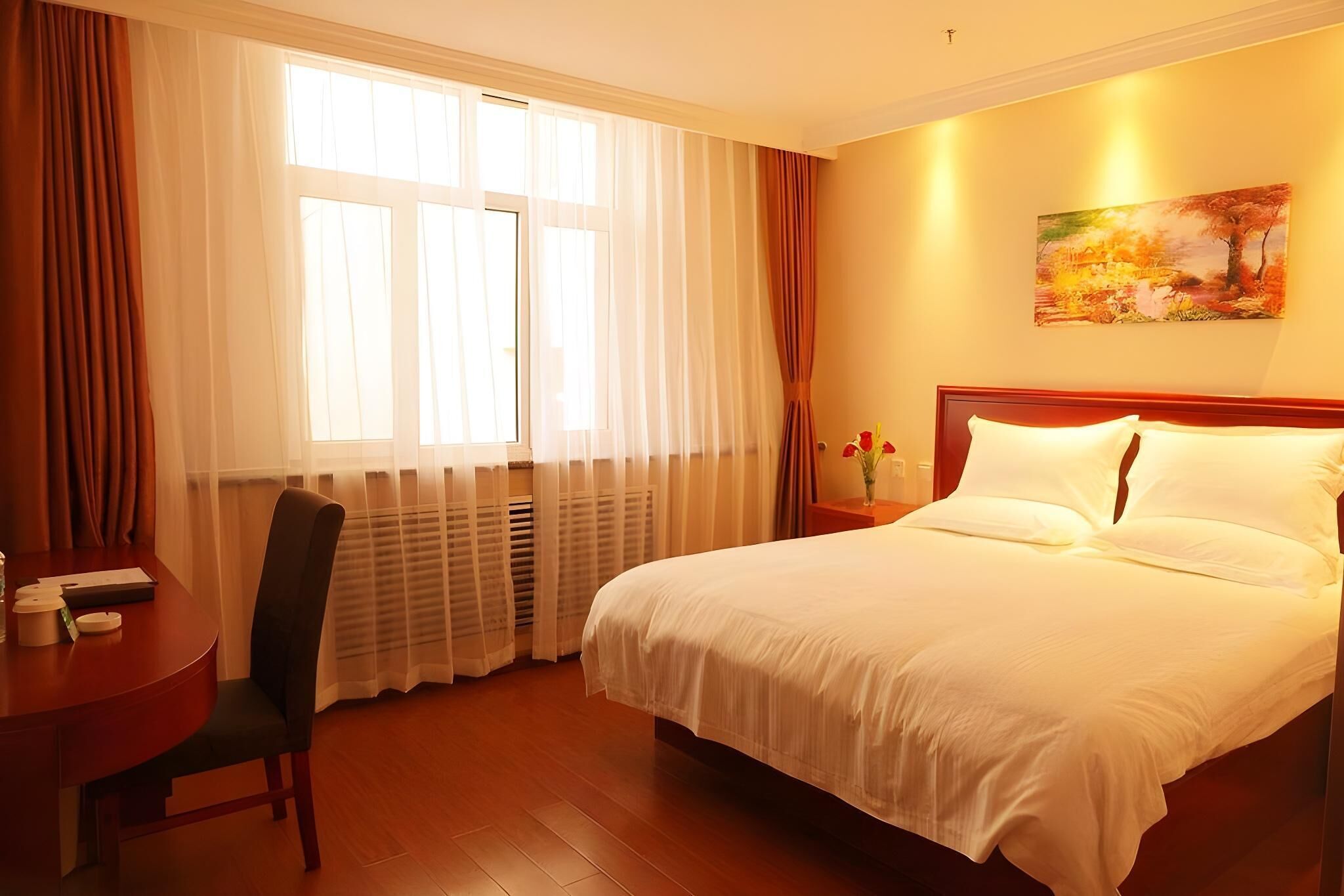 Una habitació d'hotel amb un llit gran, un escriptori amb una cadira, una finestra amb cortines i un quadre a la paret.
