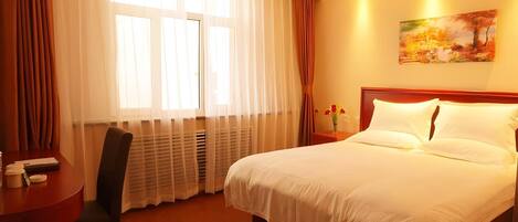 Una habitació d'hotel amb un llit gran, un escriptori amb una cadira, una finestra amb cortines i un quadre a la paret.