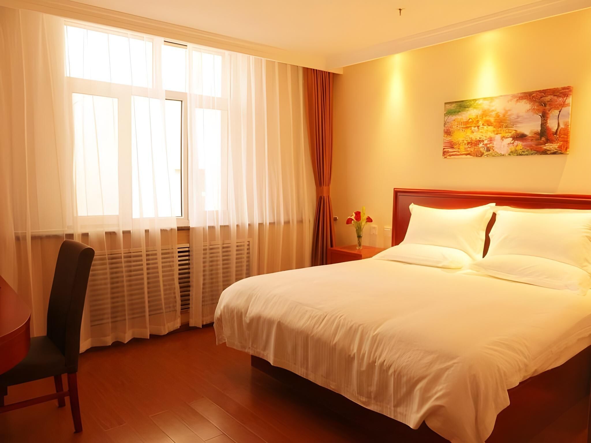 Habitación de hotel con cama, una silla, una mesita de noche, un cuadro en la pared y una ventana con cortinas.