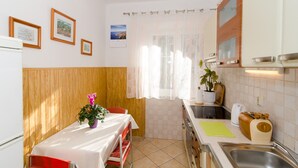 A compact kitchen with a dining table, a potted plant, and a window with sheer curtains. - Apartman Red Orange (Dubrovnik)