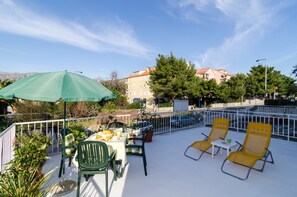 A terrace with outdoor seating, a table with food, and a view of buildings and trees. - Apartman Red Orange (Dubrovnik)