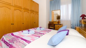 A hotel room with a large wooden wardrobe, a bed with a floral bedspread, a desk with a chair, and a mirror. - Apartman Red Orange (Dubrovnik)