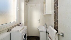 A compact bathroom with a washing machine, a sink, and a toilet. - Apartman Red Orange (Dubrovnik)