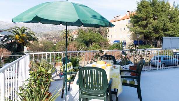 A balcony with a table set for two, chairs, a green umbrella, and potted plants. - Apartman Red Orange (Dubrovnik)