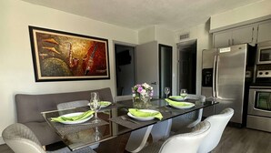 Un moderno comedor con una mesa de vidrio, sillas blancas acolchadas y un cuadro en la pared.