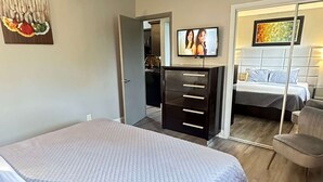 Un dormitorio moderno con una cama grande, televisor, cómoda y espejo.