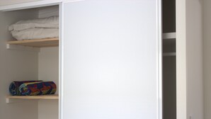 Une armoire blanche à deux étagères ; sur la première étagère se trouve une couverture blanche pliée, et sur la deuxième, une couverture colorée enroulée.