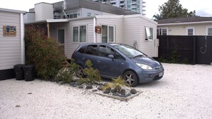 Une voiture compacte est garée sur une allée de gravier, avec un petit jardin et un bâtiment en arrière-plan.