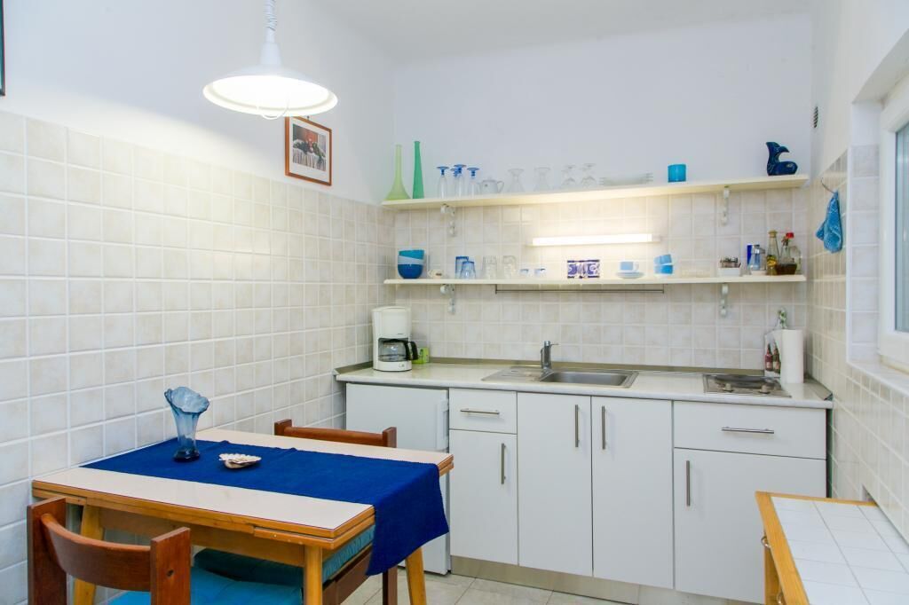 A compact kitchen with white cabinets, a coffee maker, and a sink. There is a dining table with a blue tablecloth and chairs.