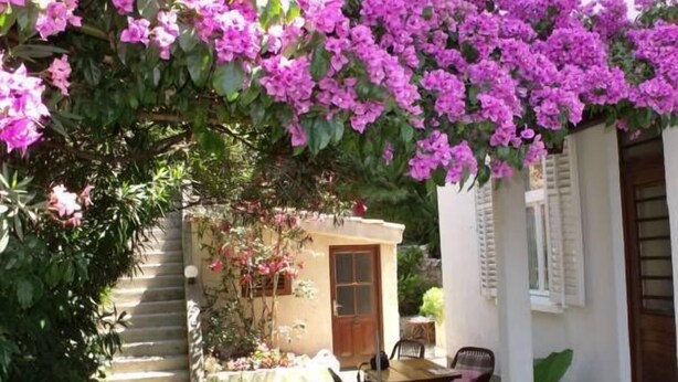 A patio with a table and chairs, surrounded by lush greenery and vibrant pink flowers. - Plavi Zal (Dubrovnik)