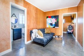 A modern living room with a grey sofa, wooden walls, a large abstract painting, and a hallway leading to a bathroom. - The Cod 'Ole The Fishermans Utopia (Agnes Water)