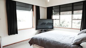 A bedroom with a bed, a television, and large windows with black curtains.