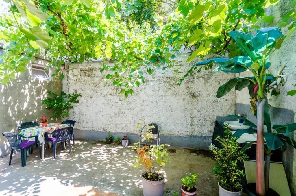 An outdoor patio with a table and chairs, surrounded by potted plants and a concrete wall.