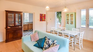 Una sala de estar acogedora con un sofá azul claro, una mesa de comedor con sillas blancas, un mueble verde y un aparador de madera con puertas de cristal.