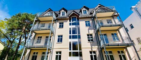 A multi-story residential building with balconies, large windows, and a central entrance.
