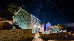 A stone building with a gated entrance, a pool area, and a starry night sky. - Holiday Home Rustic (Muc)