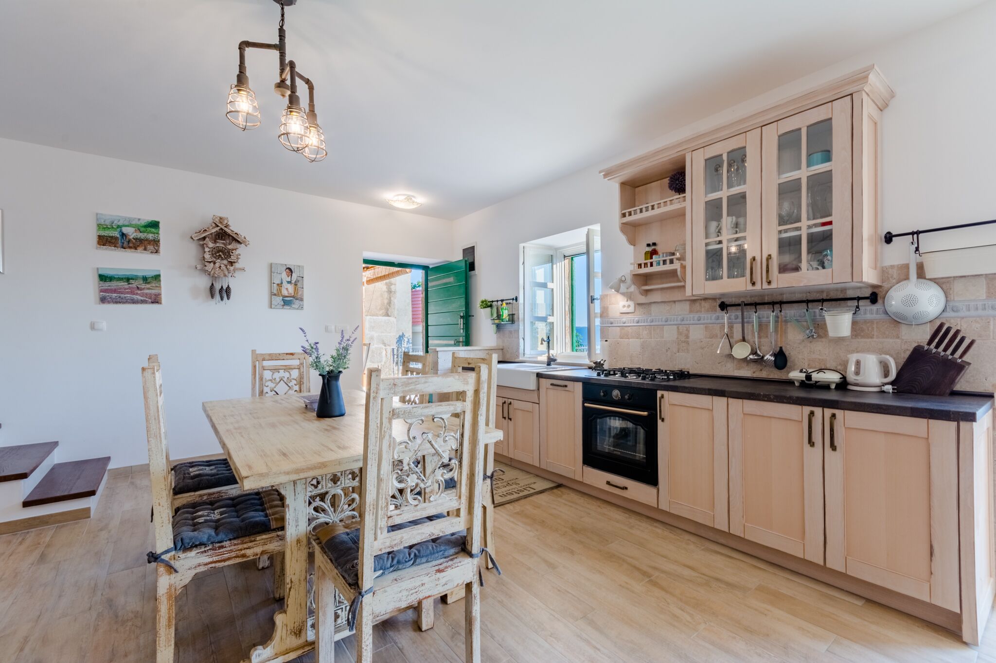 A modern kitchen with wooden cabinets, a dining table with chairs, and a hanging light fixture.