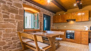 Une cuisine rustique avec des murs en pierre, des armoires en bois et une grande table en bois accompagnée de bancs.