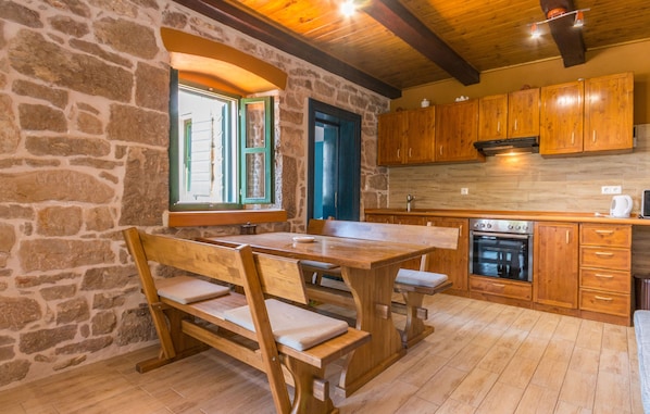 A rustic kitchen with stone walls, wooden cabinets, and a large wooden table with benches. - Apartment Porat (Drage)