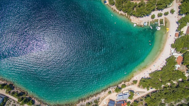 Une vue aérienne d’une zone côtière avec une plage dégagée, des bateaux et des bâtiments.