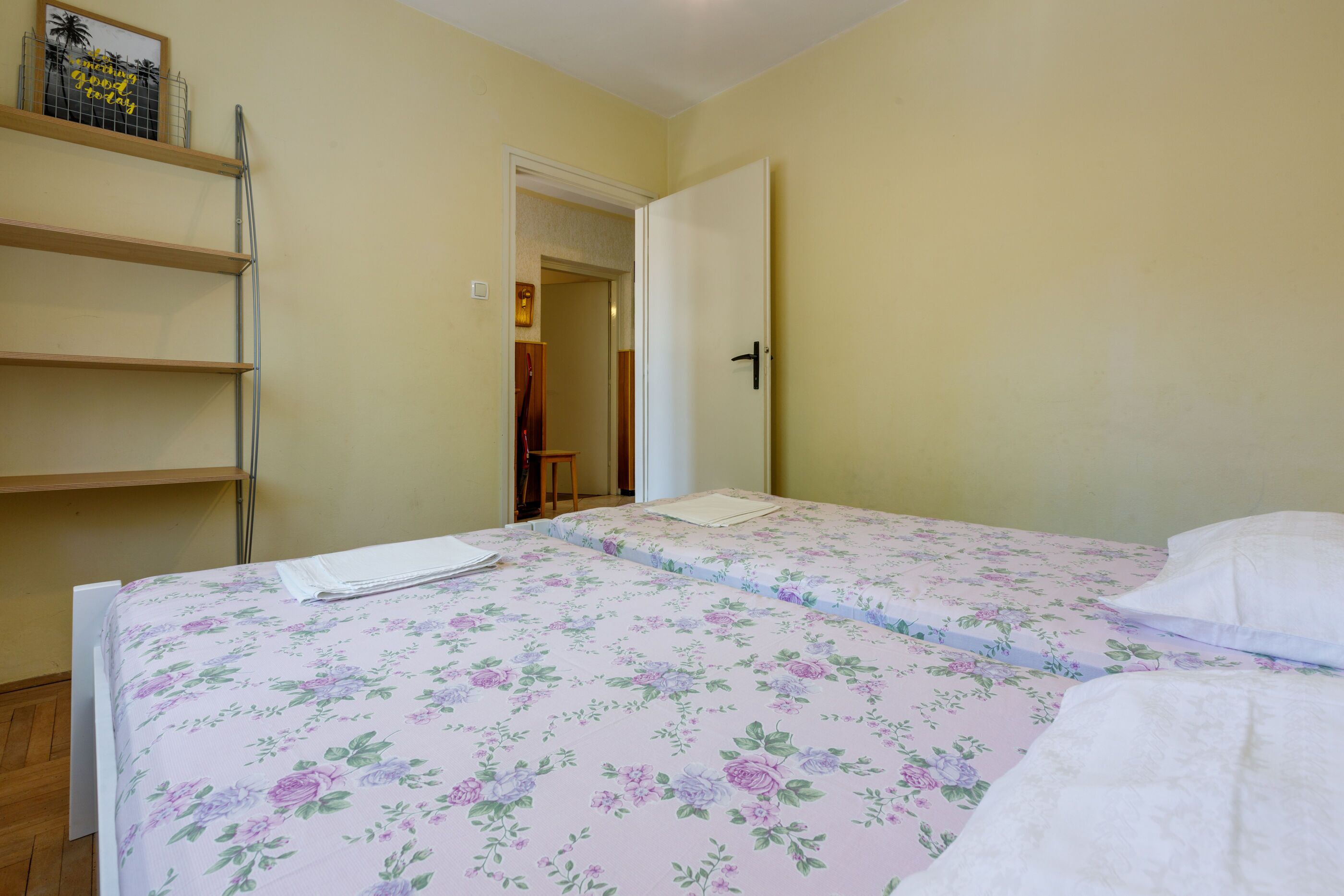 A bedroom with a bed, a shelf, and a door leading to another room.