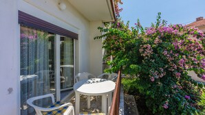 A patio with a table and chairs, a glass door, and a flowering bush. - Apartment Eugen (Crikvenica)